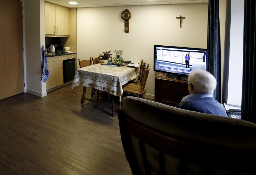 Oudere man zittend in een comfortabele stoel kijkt naar de tv in zijn zorgappartement.